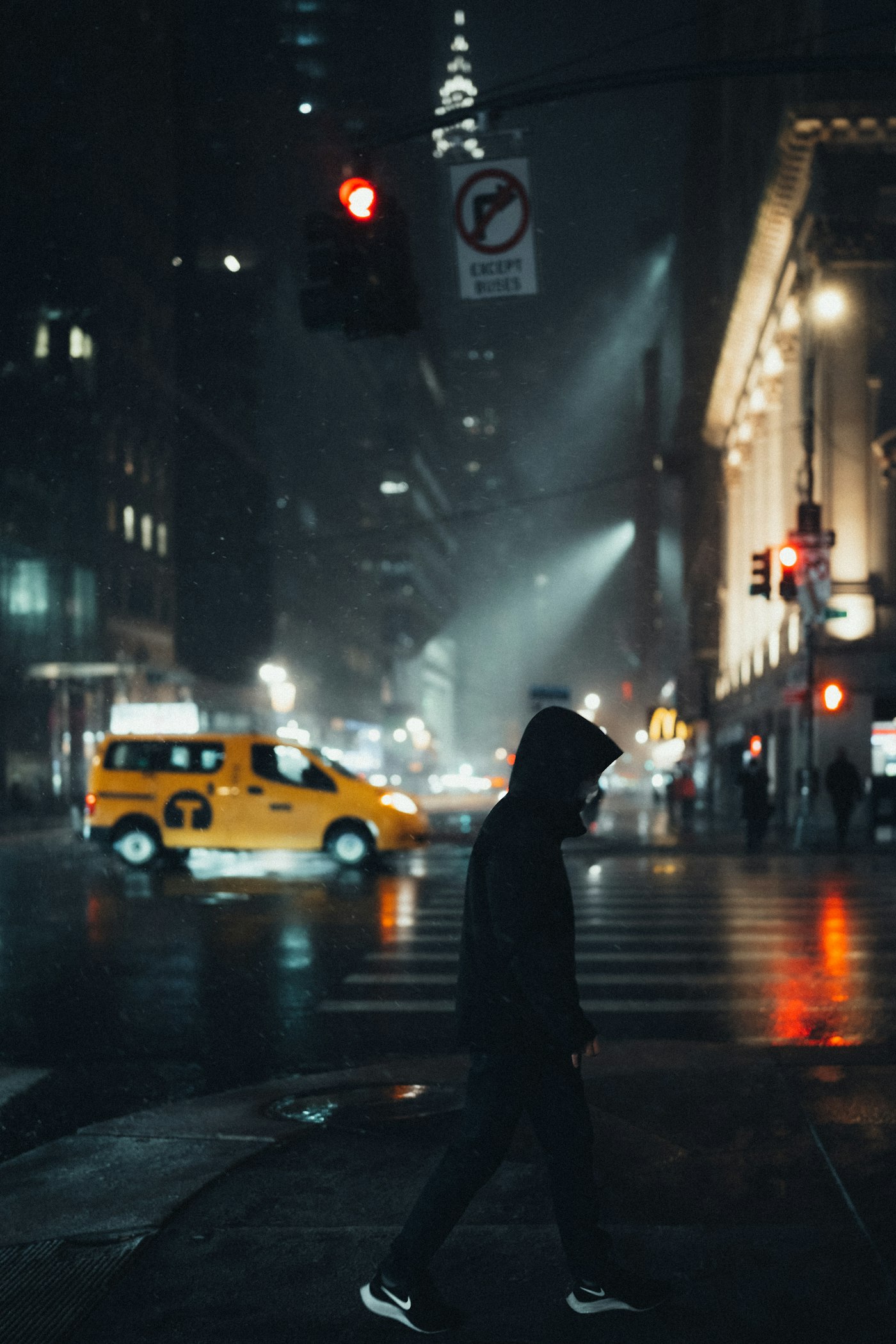 Pessoa de moletom preto atravessando uma rua à noite.